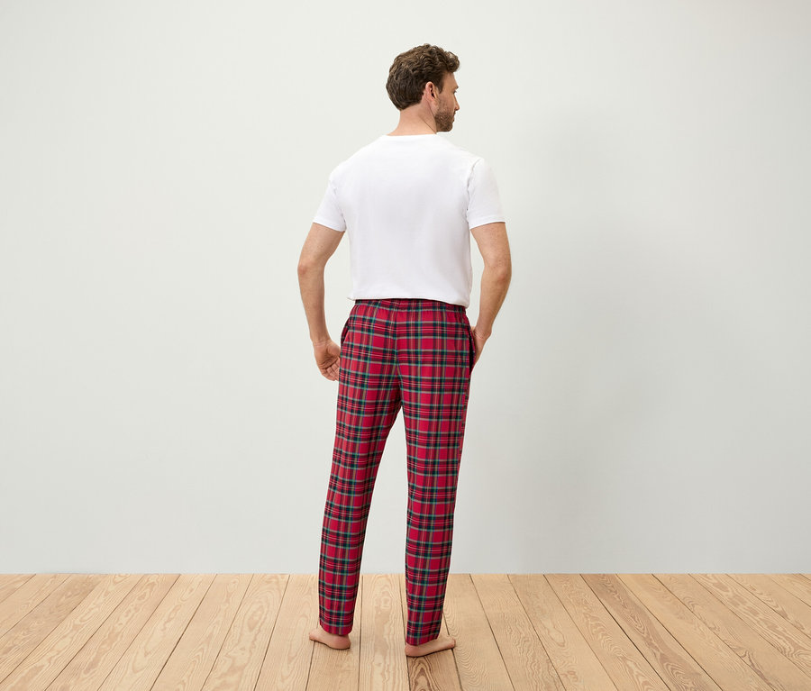 Háttal a kamerának egy férfi piros kockás pizsamanadrágban, fehér pólóban, kezét a zsebébe téve.