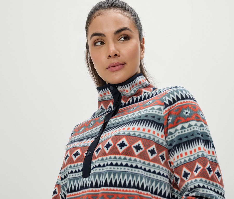 Portré egy barna hajú nőről, aki egy sokszínű, geometrikus mintás fleece felsőt visel.