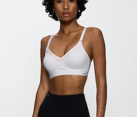 Nő visel egy rózsaszín részletekkel ellátott fehér sportmelltartót és fekete leggingset.