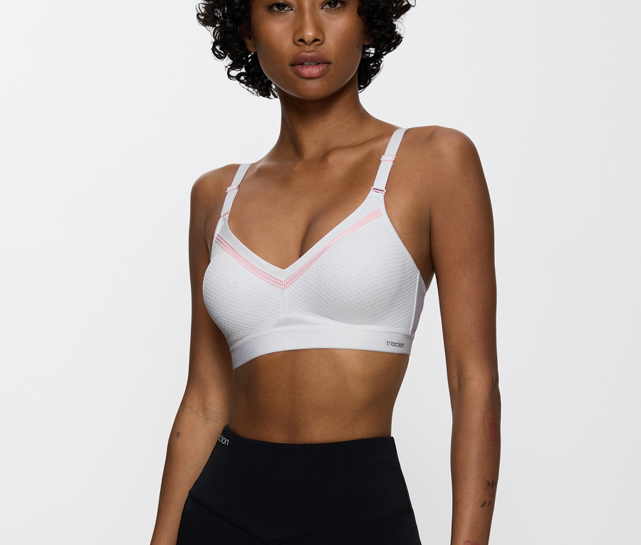 Nő visel egy rózsaszín részletekkel ellátott fehér sportmelltartót és fekete leggingset.