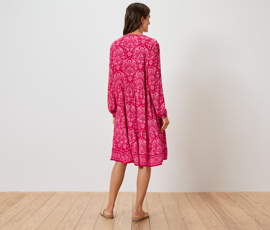 Hátulnézet egy virágmintás, rózsaszín, térdig érő ruhát és szandált viselő nőről.