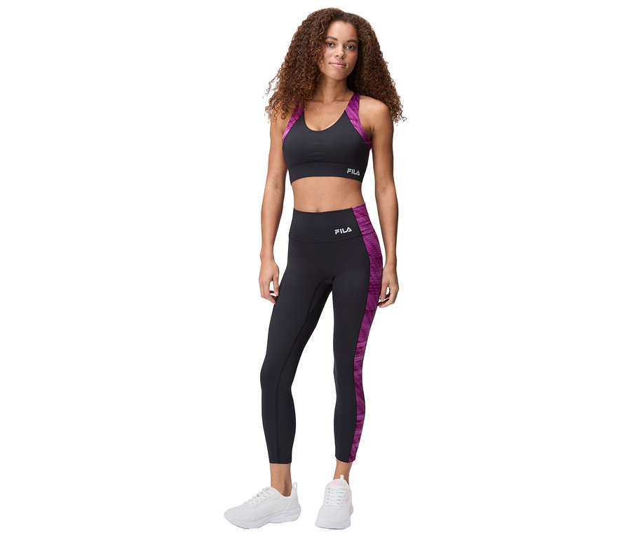Nő áll fekete Fila sportmelltartóban lila díszítéssel és leggingsben, fehér sportcipővel.
