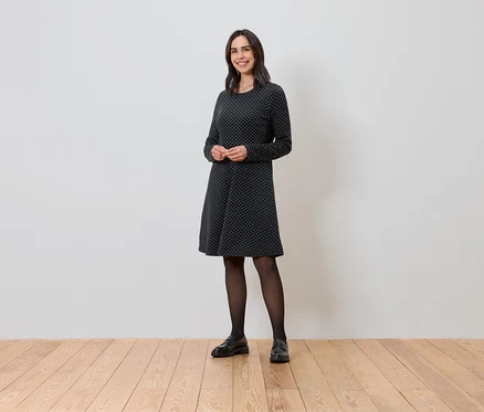 Nő áll és csillogó jacquard ruhát visel.