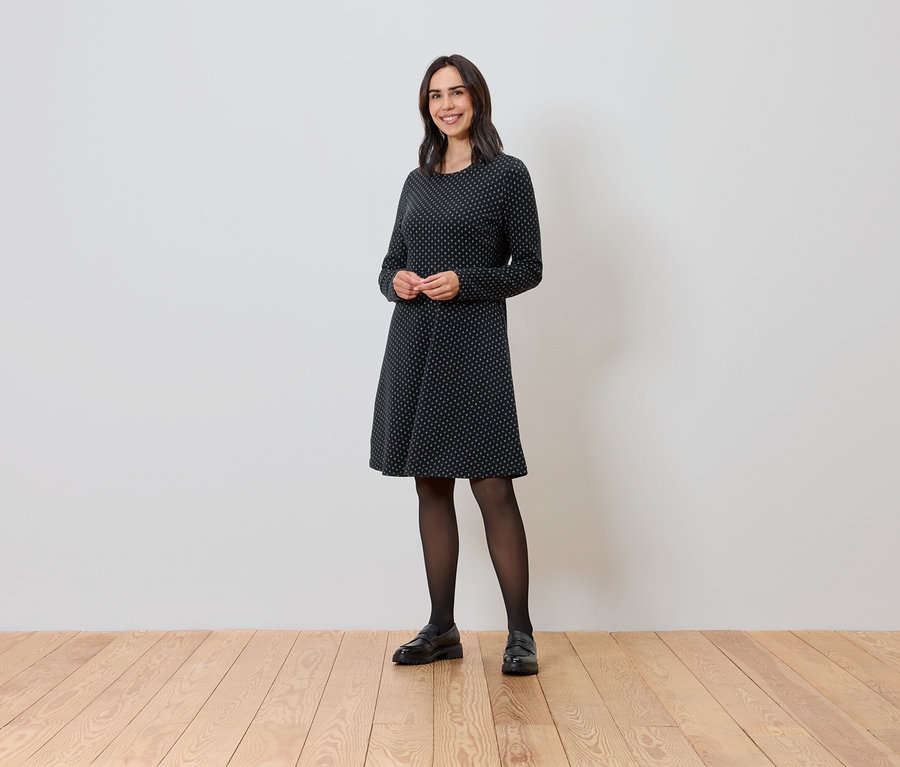 Nő áll és csillogó jacquard ruhát visel.