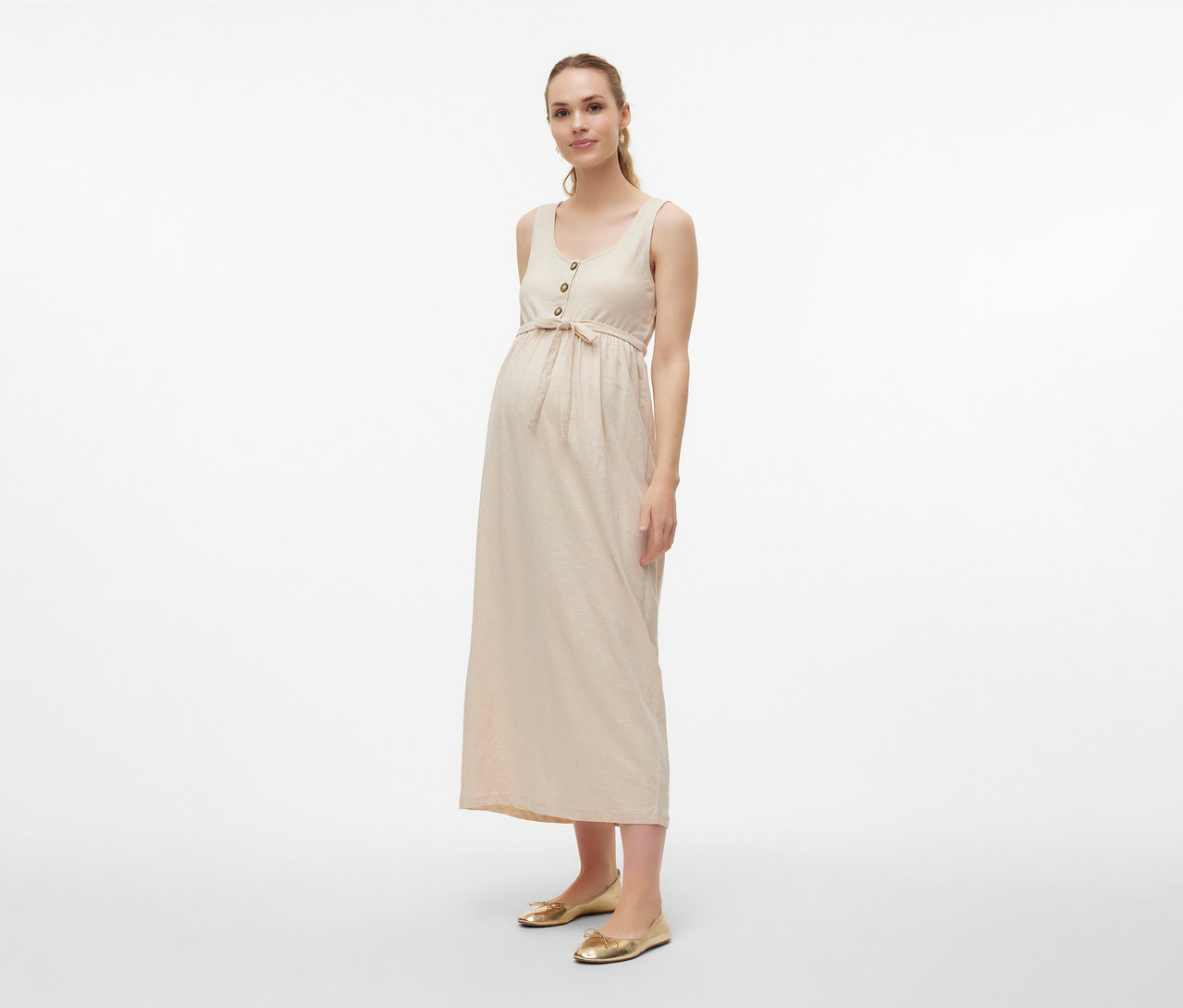 Nő visel MAMALICIOUS »MLEVI LIA« kismamaruhát övvel és arany balerinacipőt világos háttér előtt.