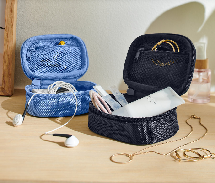 Az asztalon két nyitott, kis tárolótáska áll, egy kék fülhallgatóval, egy sötét pedig bőrápolási termékekkel és ékszerekkel.