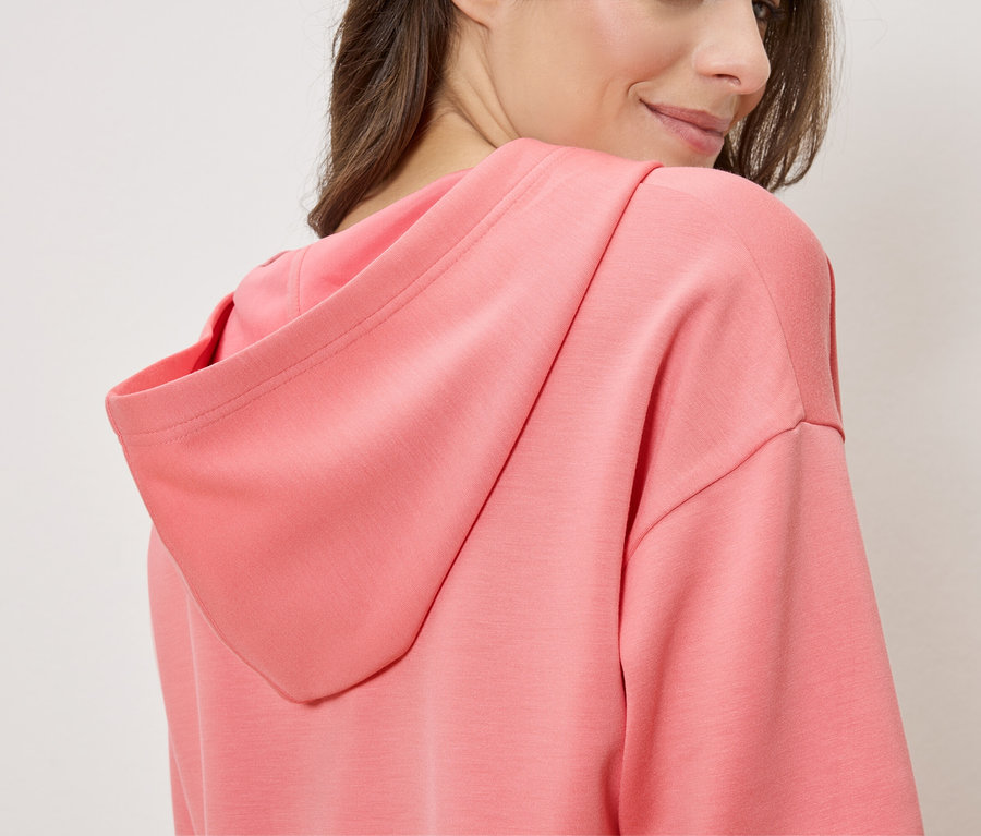 Nő lazacszínű kapucnis pulóvert visel, oldalról nézve.