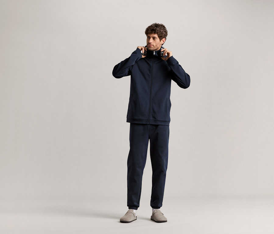 Férfi áll és fejhallgatót tart a kezében, sötétkék Férfi szabadidő szett van rajta.