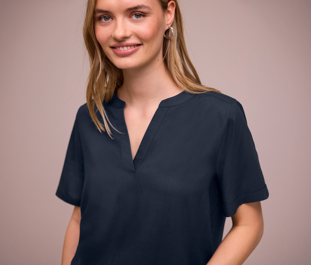 Nő visel egy sötétkék Street One blúzt V-nyakkivágással és ezüst fülbevalót.