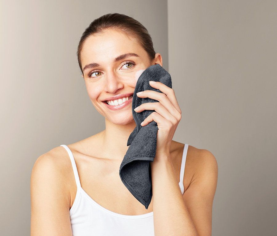 Nő tisztítja az arcát egy szürke, 3 darabos mikroszálas kozmetikai kendővel.