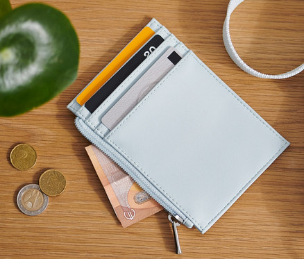 Egy fa asztalon egy világoskék pénztárca, érmék és egy táska látható.