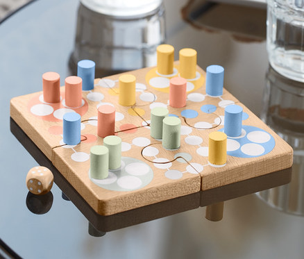 Az asztalon egy Ludo-puzzle társasjáték, fa színes bábukkal és egy kockával.