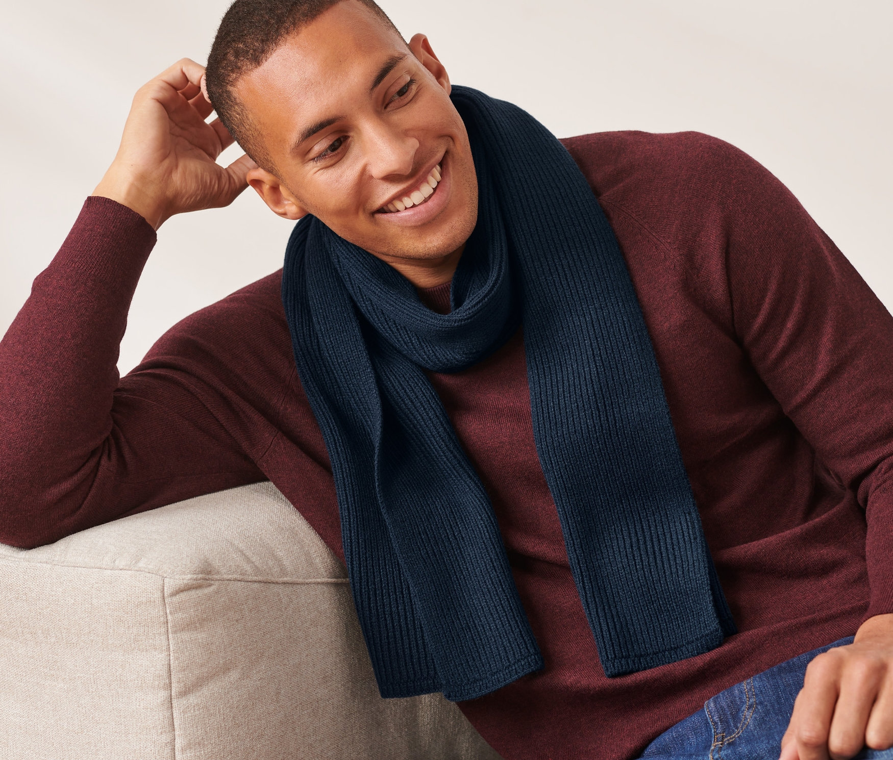 Egy férfi ül a kanapén és sötétkék kötött sálat visel.