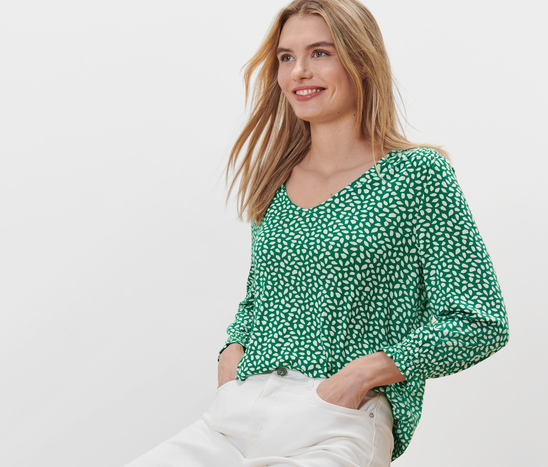 Nő ül egy széken, és zöld, mintás pólóblúzt visel.