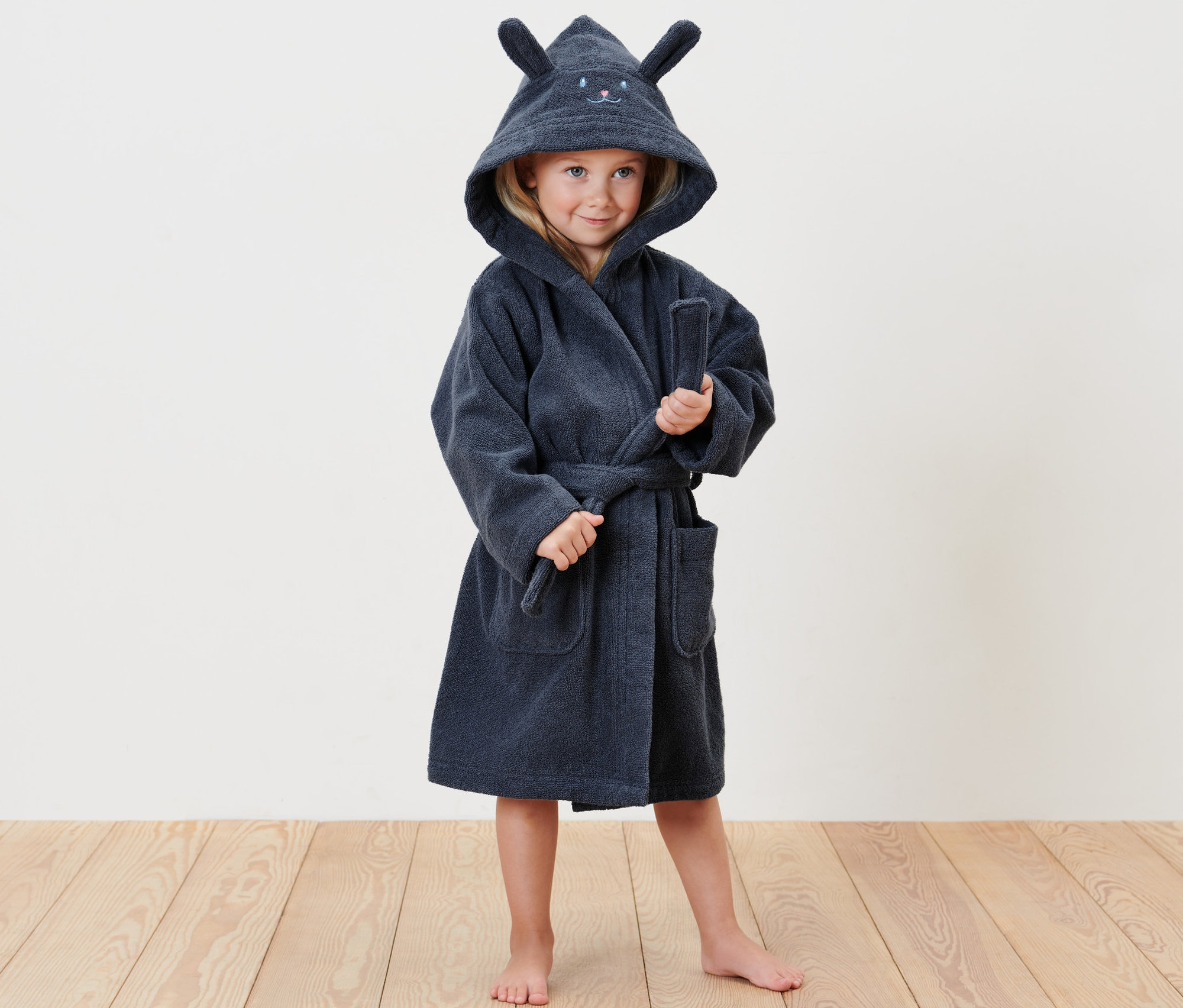 Egy mezítlábas lány áll egy sötétkék, nyuszis gyerek fürdőköpenyben.