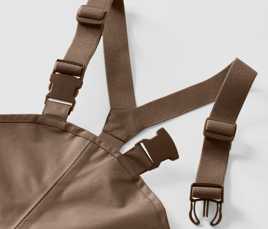 Egy gyermek esőnadrág részlete barna, rugalmas pántokkal és műanyag csatokkal fehér háttéren.