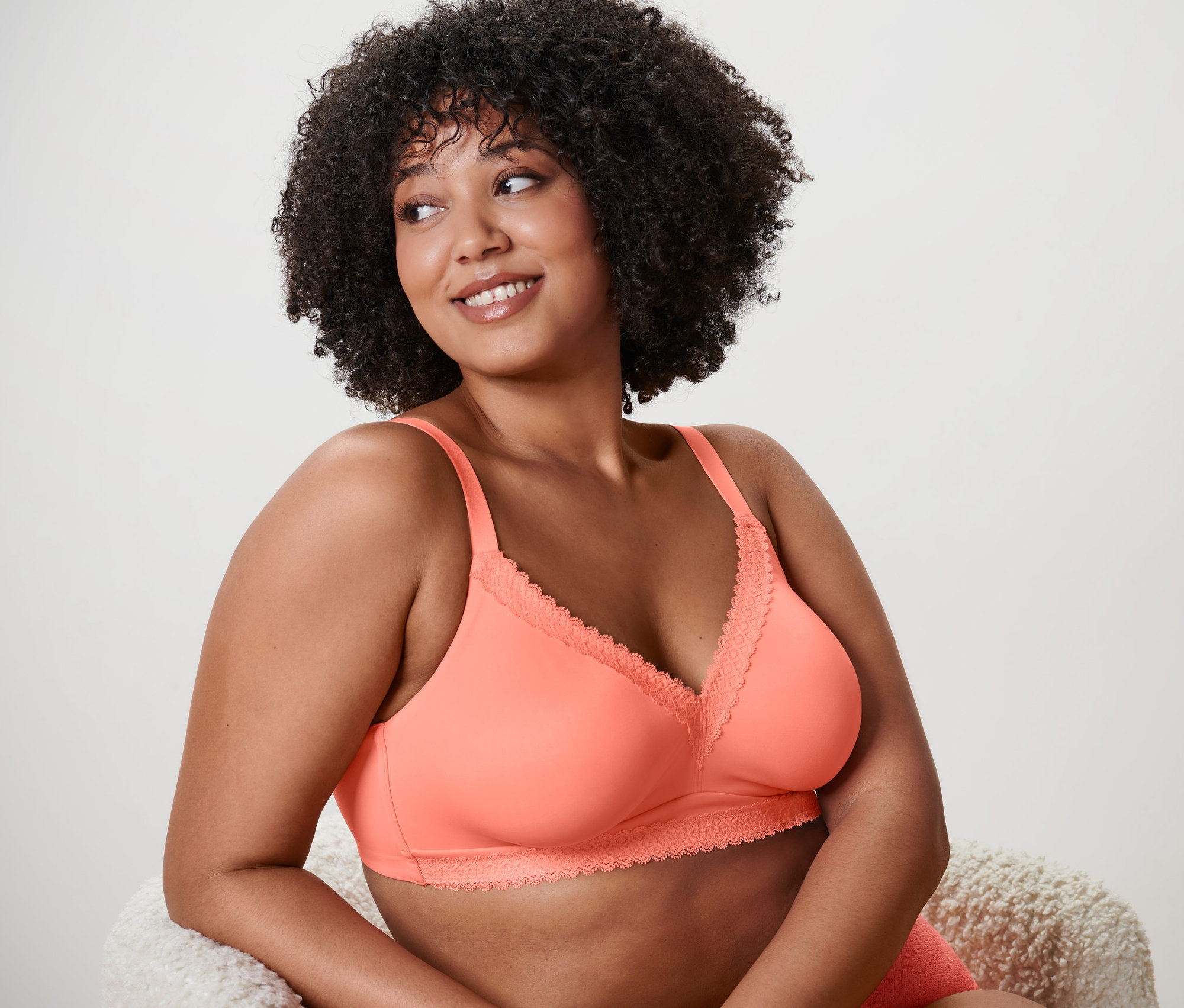 Afro frizurás nő papaya színű, csipkés, puha melltartót visel.