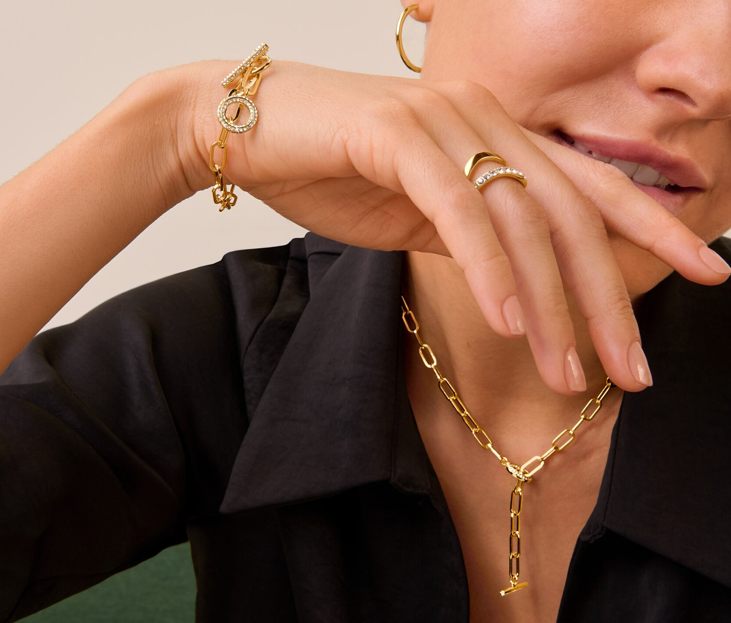 Nő visel Double Wave női gyűrűt üvegkristályokkal, női karkötőt és nyakláncot T-kapocs üvegkristályokkal és aranyszínű karikafülbevaló szettet.