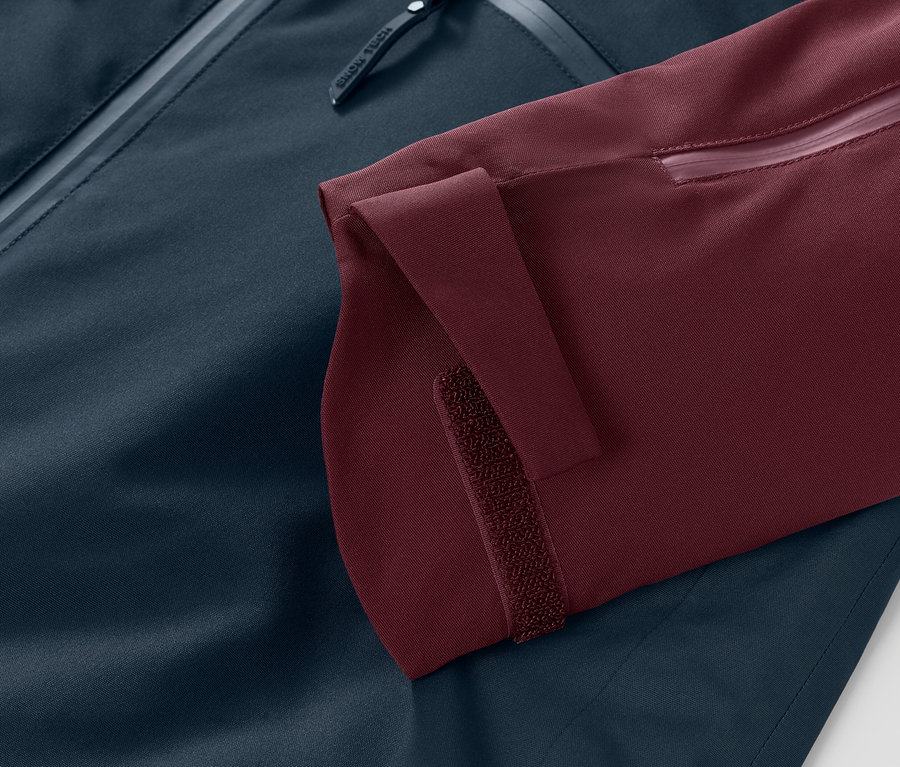 Egy női sí- és snowboardkabát (bordó/sötétkék) részlete: bordó ujjrész állítható tépőzáras mandzsettával és sötétkék kabátrész.