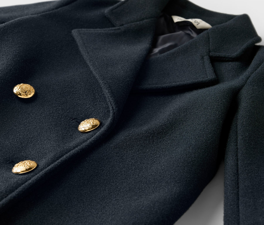 Egy sötétkék, kétsoros gombolású kabát közeli képe, arany gombokkal.