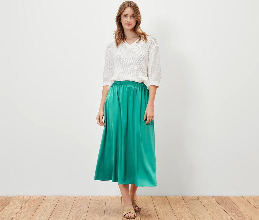 Nő pózol fehér felsőben és zöld szaténszoknyában.