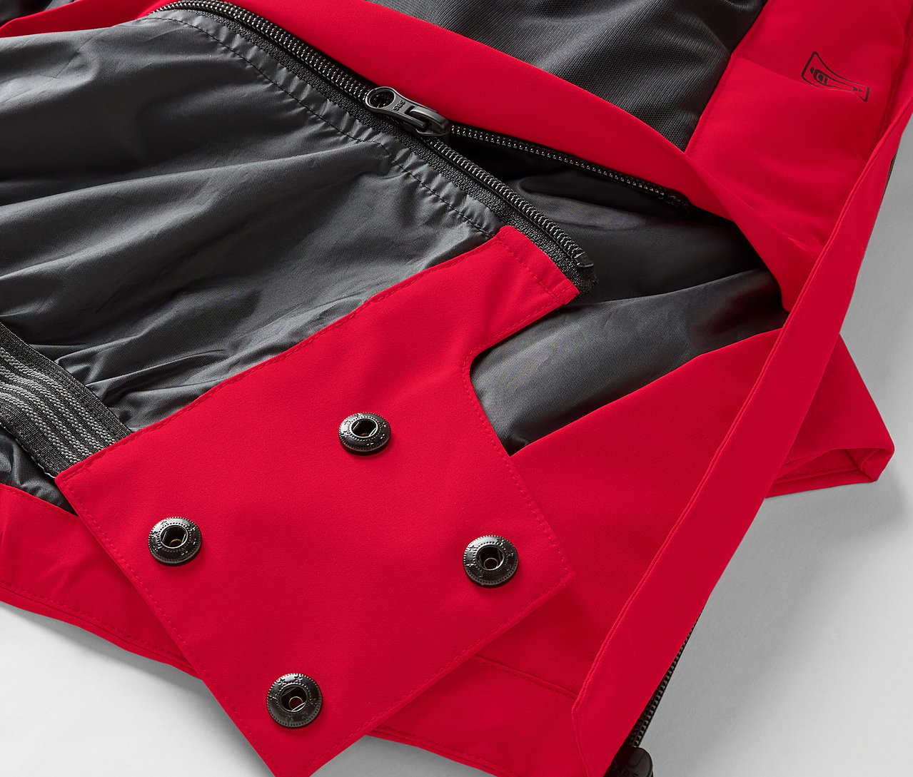 Egy piros kabát részlete fekete béléssel és patentokkal.