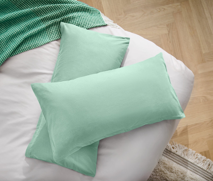 Két világoszöld párna egy fehér lepedőn egy zöld takaró mellett.