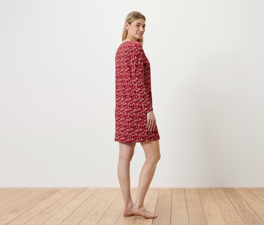 Nő áll oldalt, piros, mintás ruhát visel.