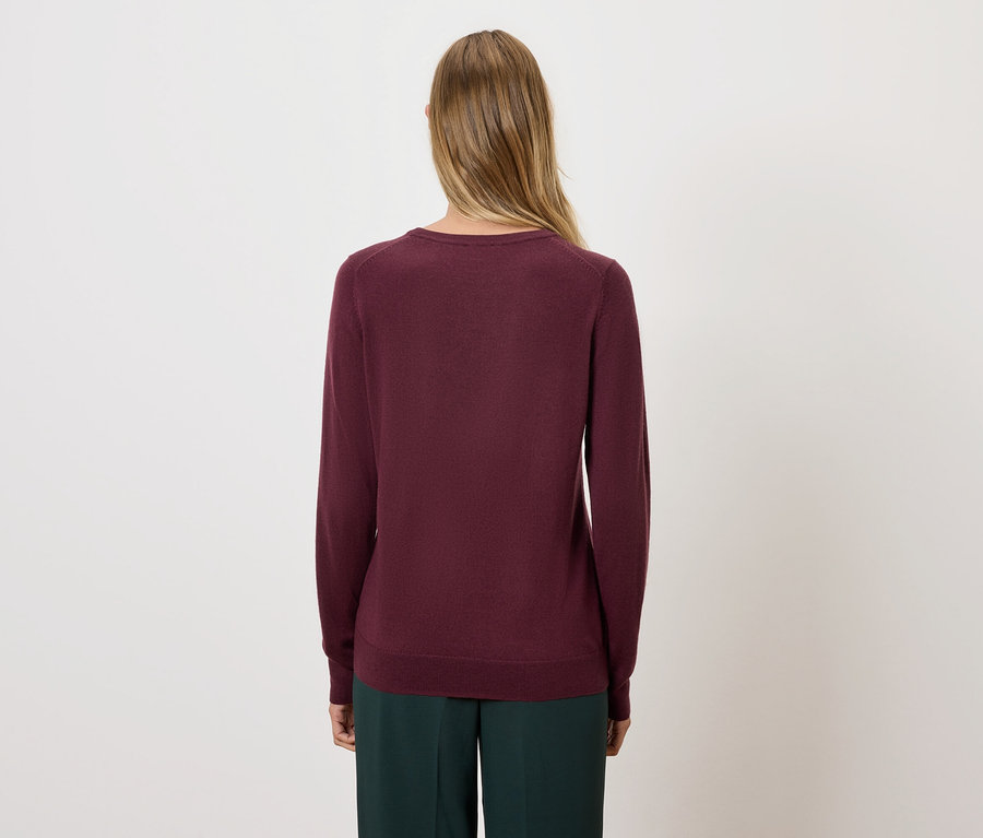 Hátulról látható egy szőke hajú nő bordó pulóverben és zöld nadrágban.