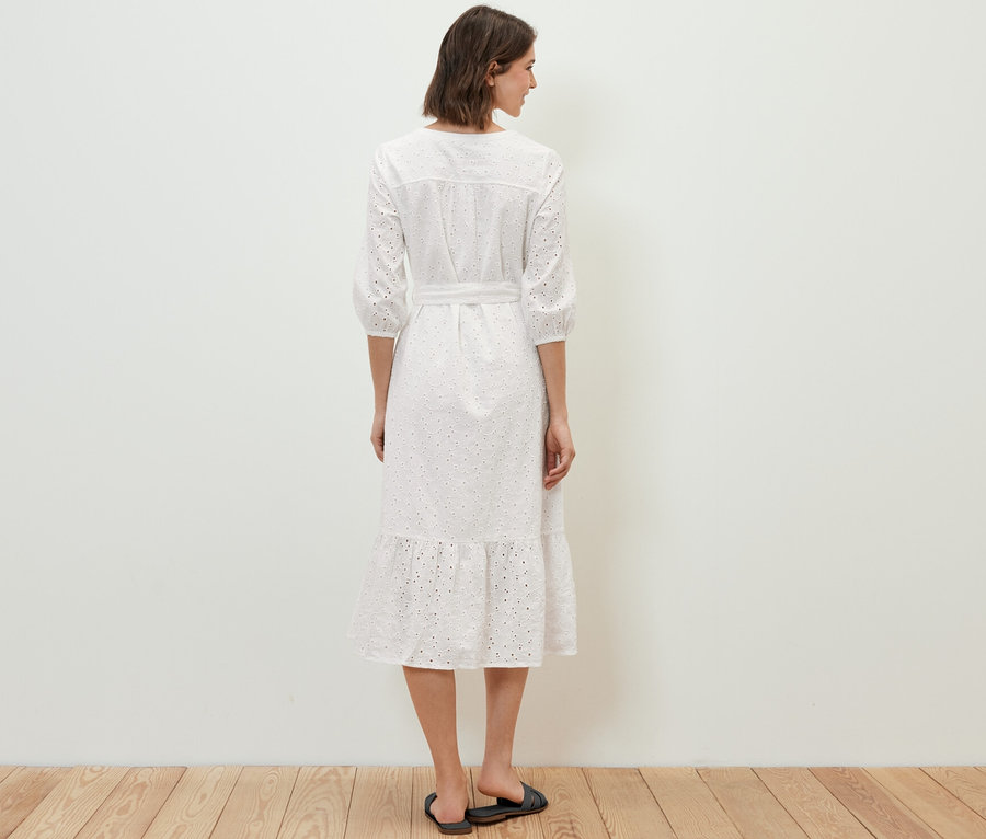 Egy nő háttal áll a kamerának, és lyukhímzéses blúzruhát visel.