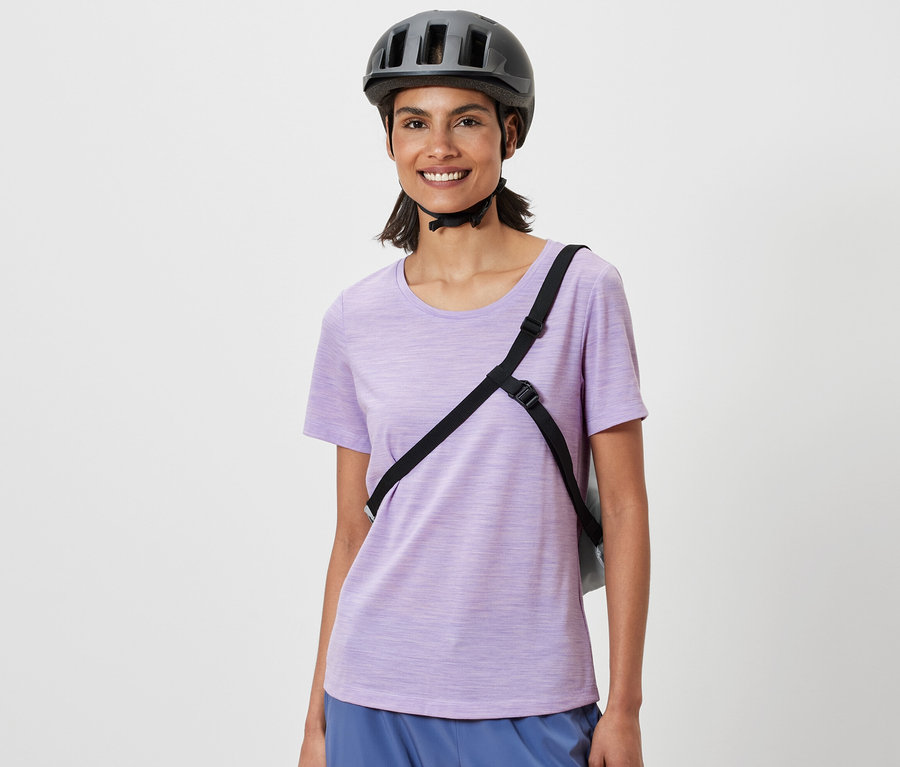 Mosolygó nő kerékpáros sisakkal és egy kerékpáros bevásárlótáskával a vállán.