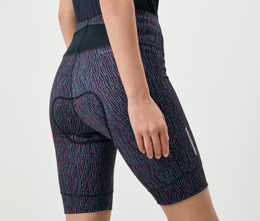 Egy nő közeli képe mintás kerékpáros rövidnadrágban, fekete derékrésszel és fényvisszaverő füllel a lábán.