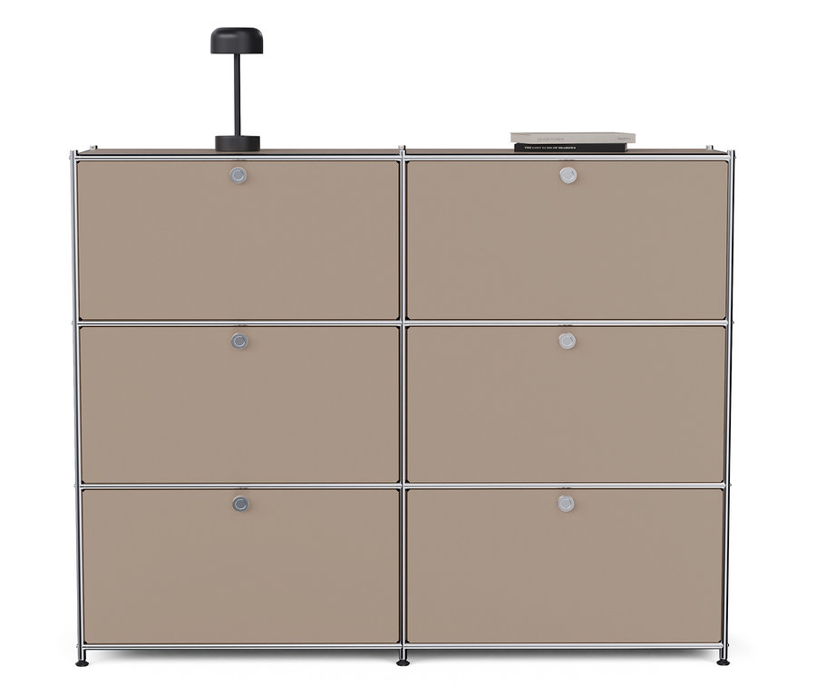 Egy szürkésbarna »CN3« fém komód hat lenyíló ajtóval áll fehér háttér előtt. A komódon egy lámpa és egy könyv található.