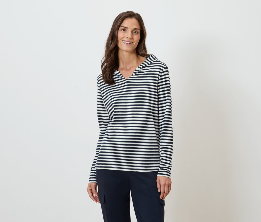 Nő visel egy csíkos, hosszú ujjú, kapucnis felsőt és egy sötétkék nadrágot.