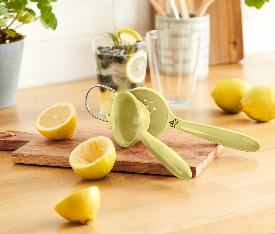 Egy fa asztalon van néhány citrom, egy citromfacsaró és egy pohár limonádé.