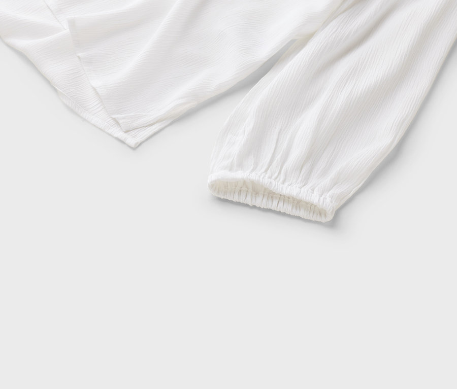 Egy fehér blúz részletes nézete hosszú ujjakkal és ráncolt mandzsettákkal fehér háttéren.