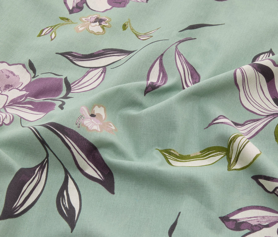 Közelkép egy mentaszínű szövetről, lila, fehér és zöld színű virágmintával.