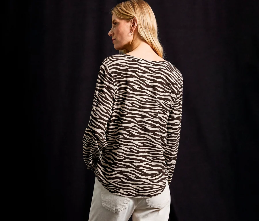Szőke nő zebra mintás Street One ingblúzt és világos farmert visel.