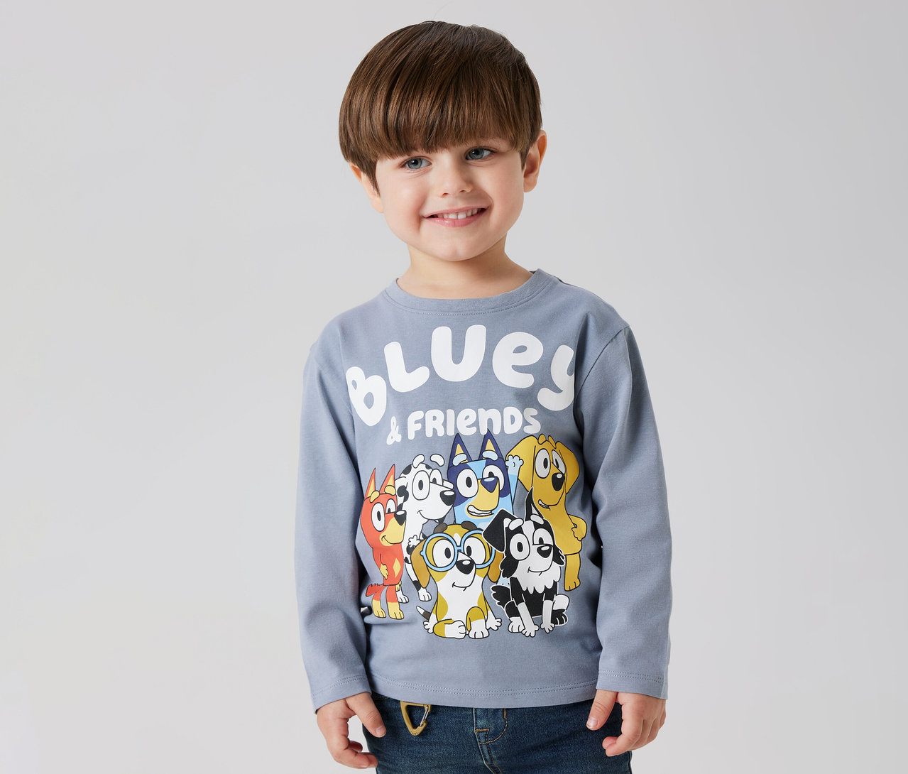 Mosolygó fiú visel egy NAME IT »BLUEY« hosszú ujjú gyerekfelsőt, Bluey és barátai mintával.