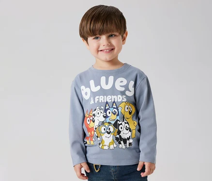 Mosolygó fiú visel egy NAME IT »BLUEY« hosszú ujjú gyerekfelsőt, Bluey és barátai mintával.