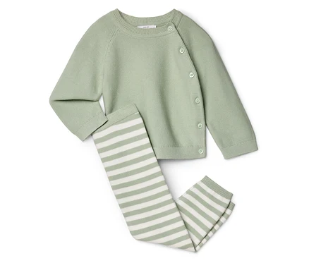 Világoszöld, gombolható kötött kardigán fekszik egy csíkos leggings mellett, fehér háttér előtt.