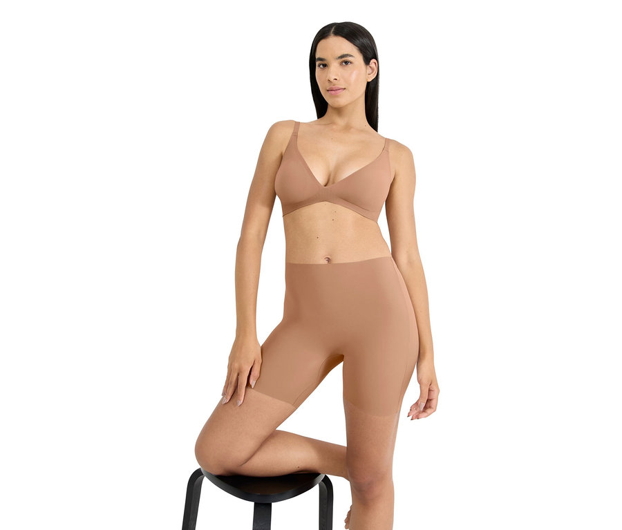 Nő pózol egy széken, testszínű melltartót és alakformáló rövidnadrágot visel.