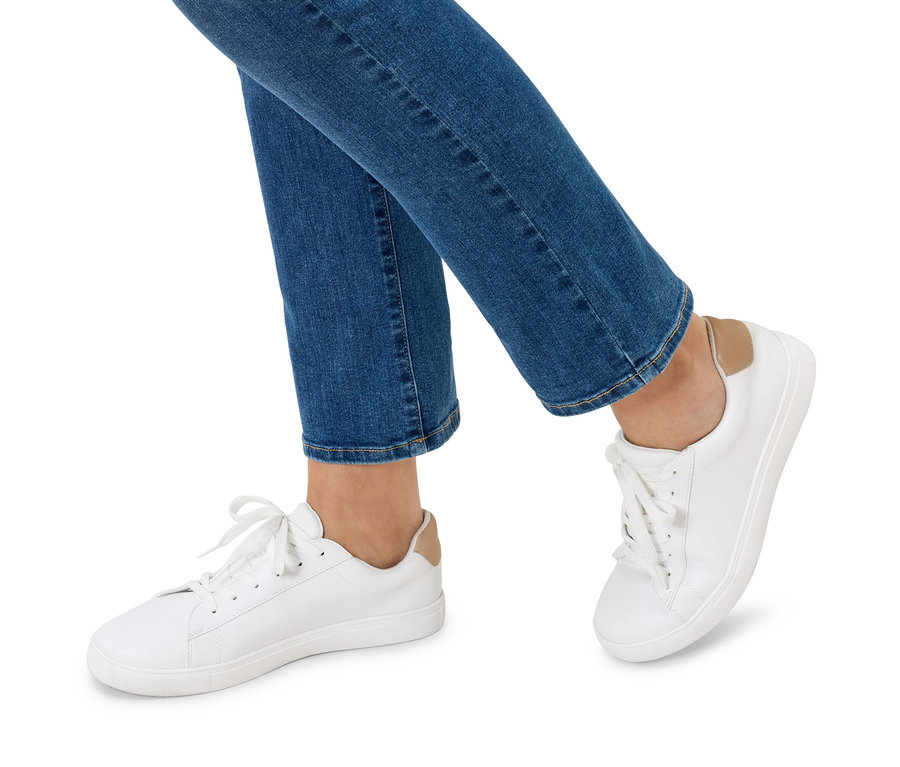 Kék farmernadrágot és fehér tornacipőt viselő személy lábai.