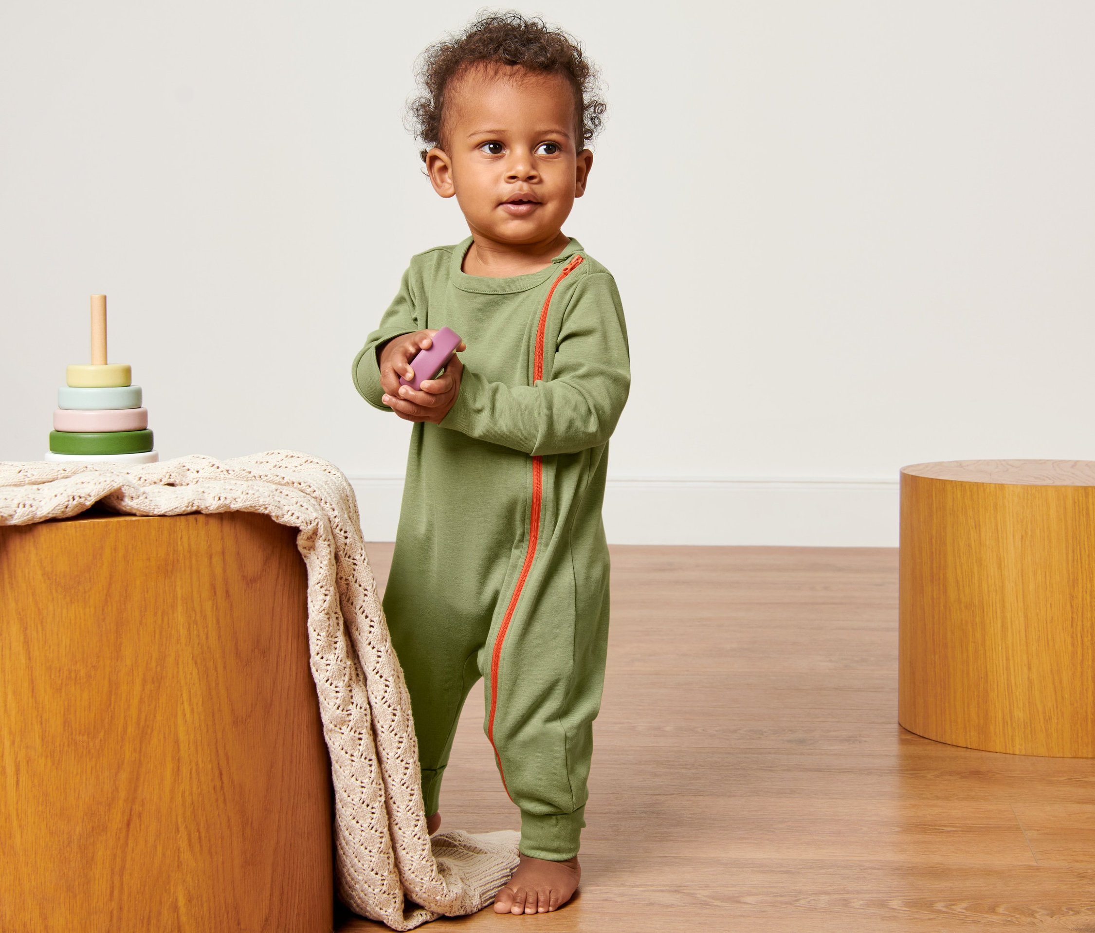 Kisgyermek zöld 2 kisgyerek egyrészes pizsama mellett áll egy fa asztalnak játékkal.