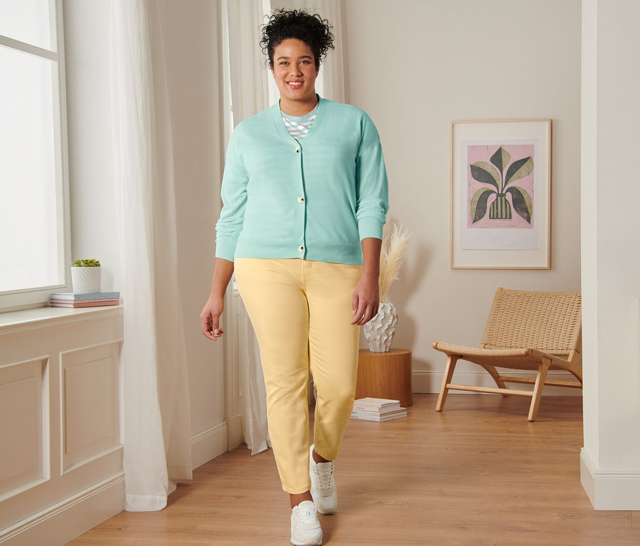 Nő sétál, menta színű csíkos pólót, V-nyakú kardigánt, sárga slim fit farmernadrágot és velúrbőr sneakercipőt visel.