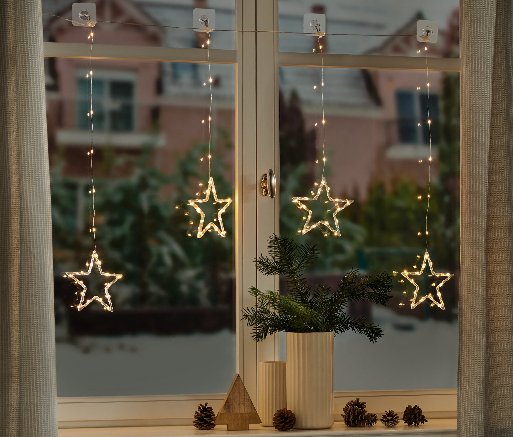 Négy LED-es fényfüggöny csillagokkal függ az ablakban.