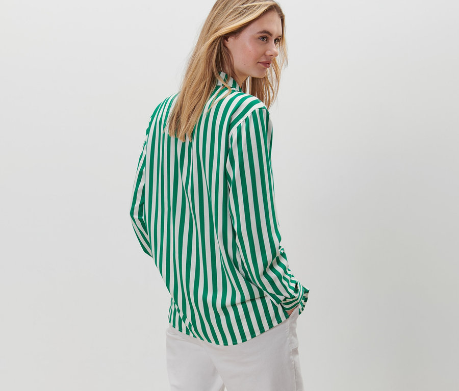 Nő pózol egy zöld-fehér csíkos blúzban és fehér nadrágban.