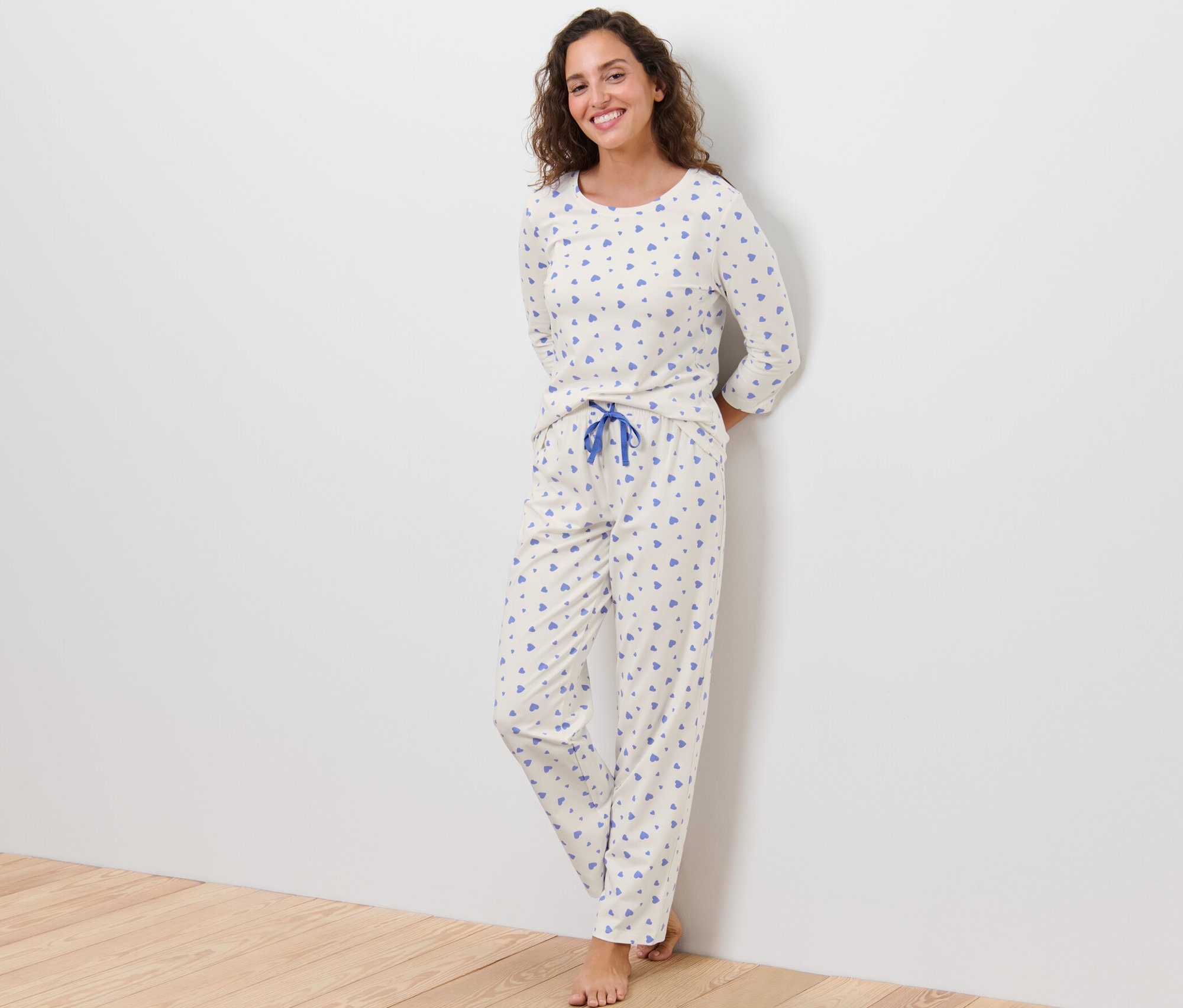 Egy nő a falnak támaszkodva szívmintás pizsamát visel.