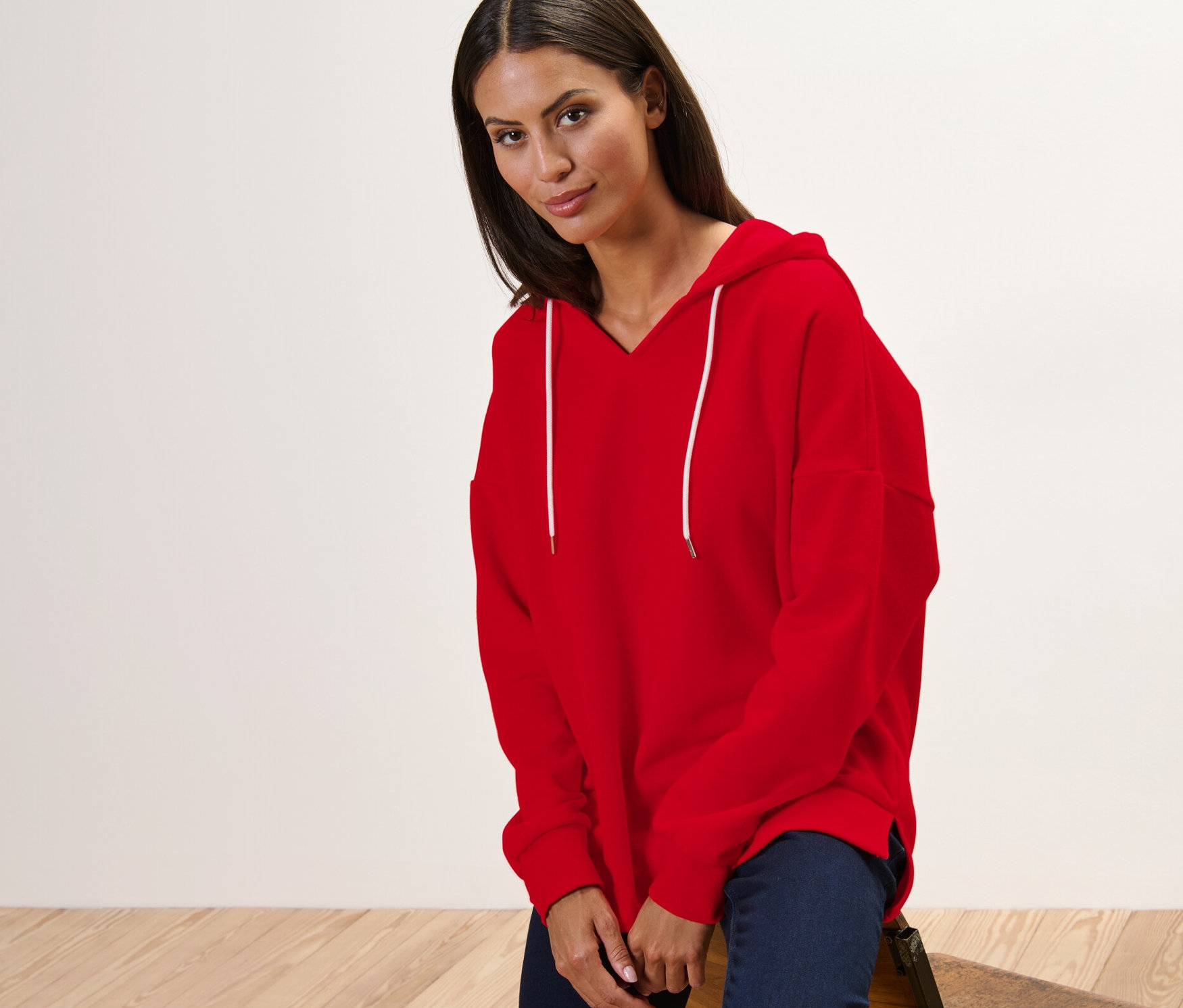 Nő ül egy széken, piros kapucnis pulóvert visel.