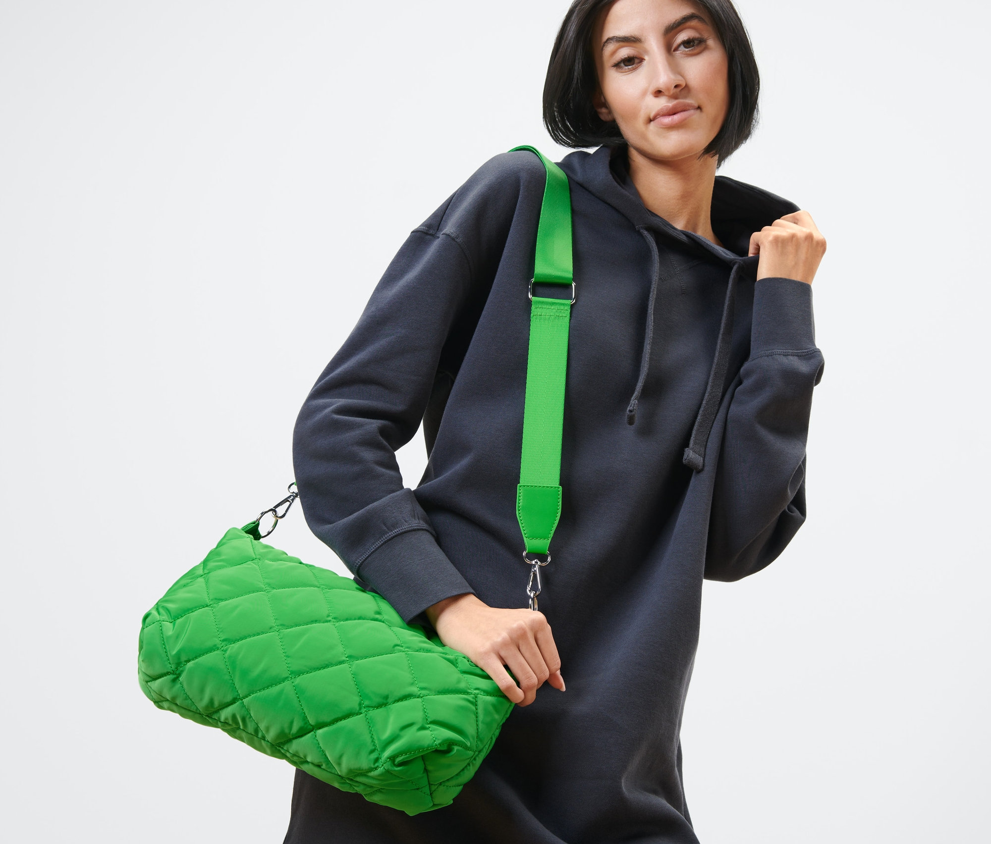 Nő pózol zöld, steppelt oldaltáskával.